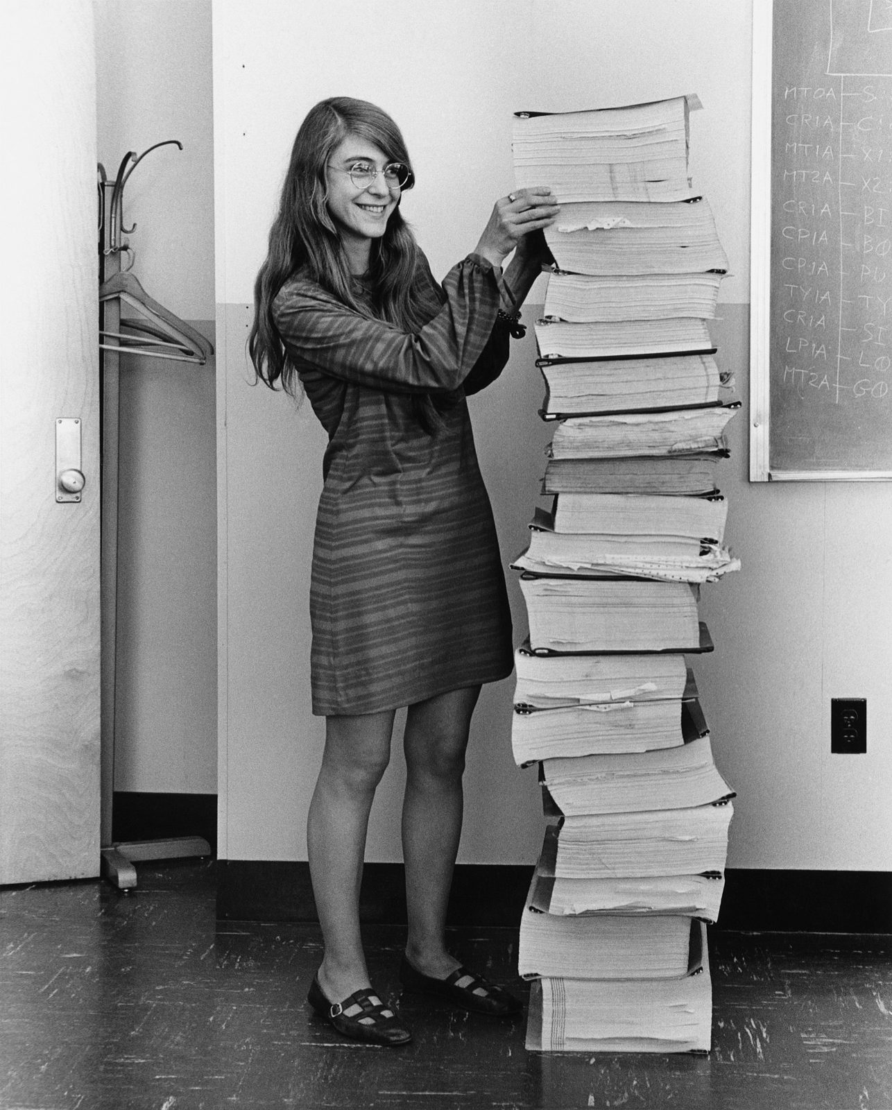 Margaret Hamilton standing beside a stack of Apollo guidance-computer code listings as tall as herself.